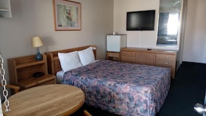 Una habitación de hotel con cama, escritorio, silla, televisión y un refrigerador pequeño.