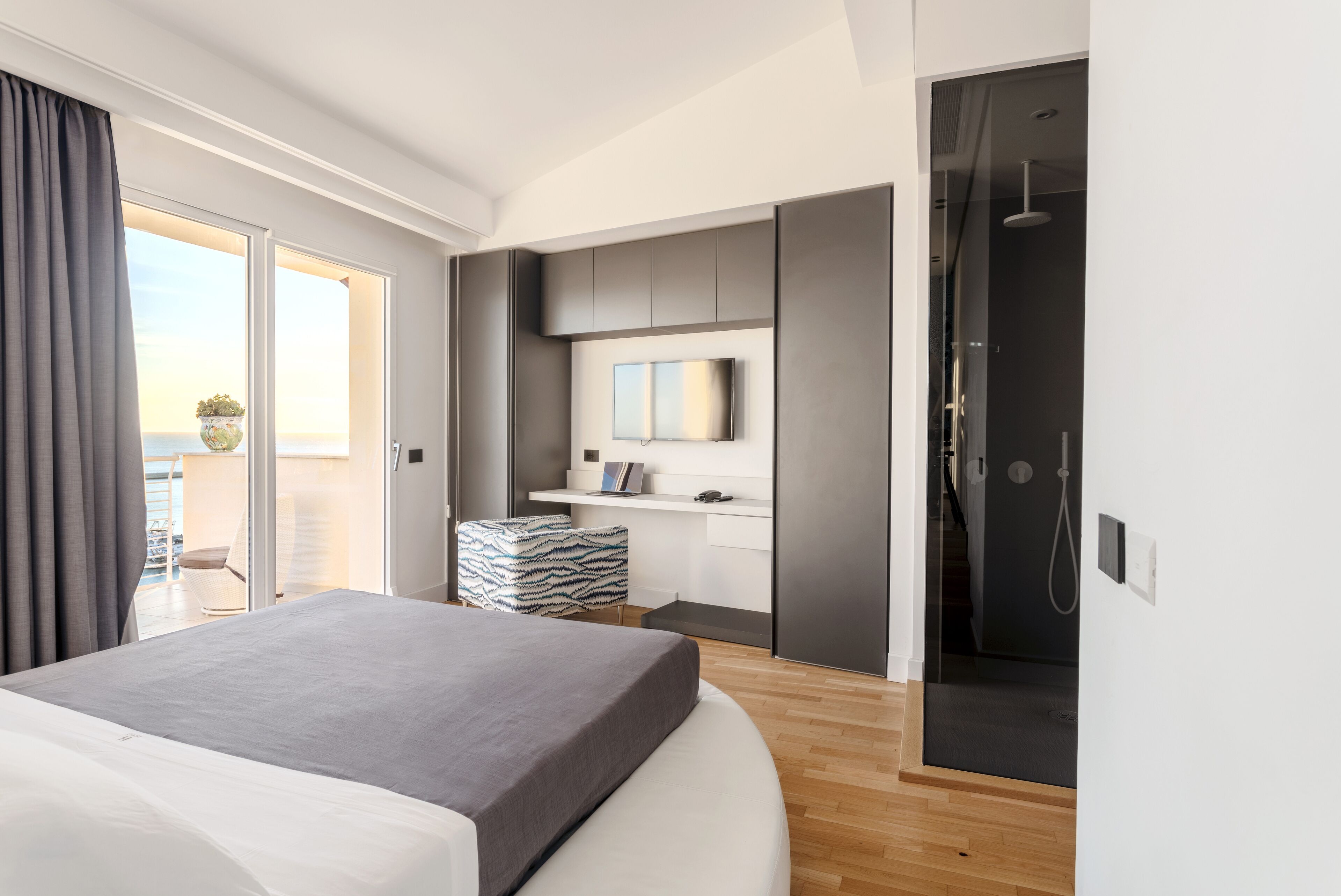 Ein modernes Hotelzimmer mit einem großen Bett, einem an der Wand montierten Fernseher, einer Duschkabine und einem Balkon mit Blick.