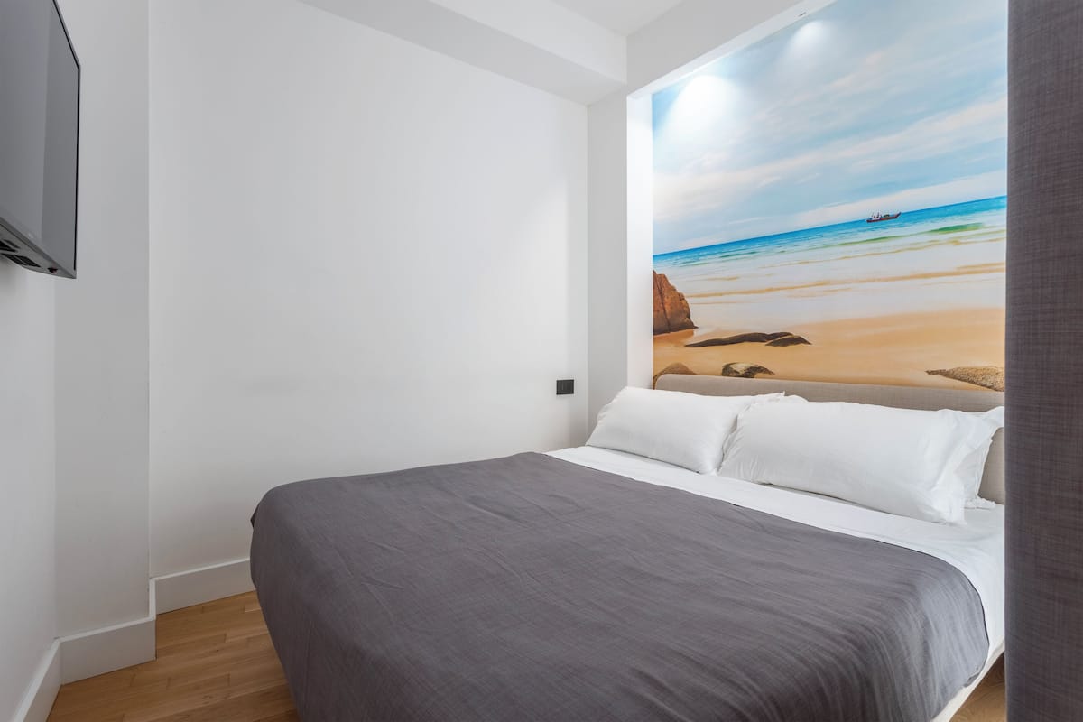 A bedroom with a bed, white walls, and a beach mural on the wall.