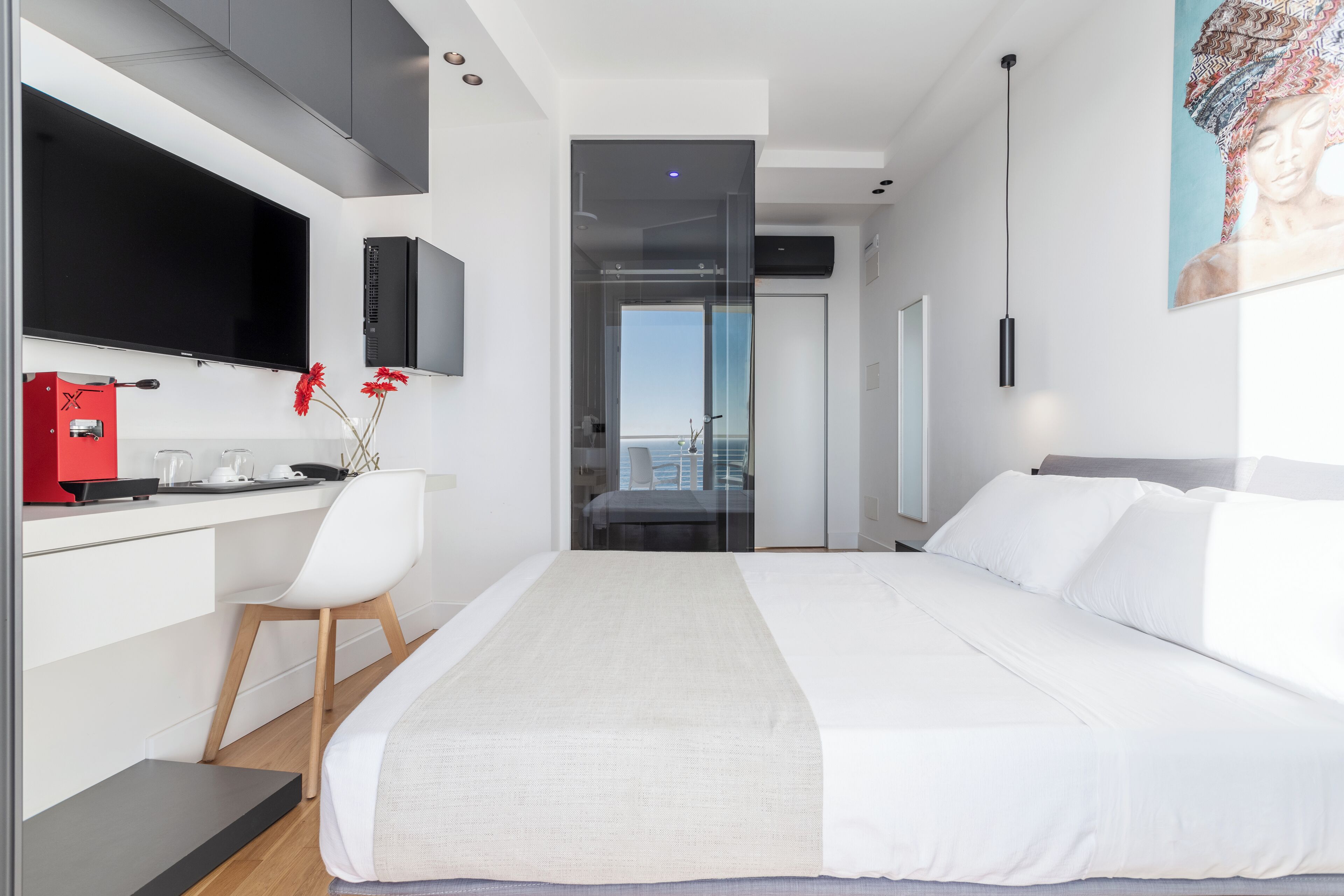 A modern hotel room with a bed, a desk with a computer, a TV, and a view of the city.