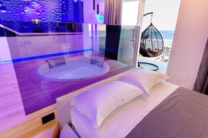 Una camera moderna con un letto, un'area salotto circolare e vista sulla spiaggia.