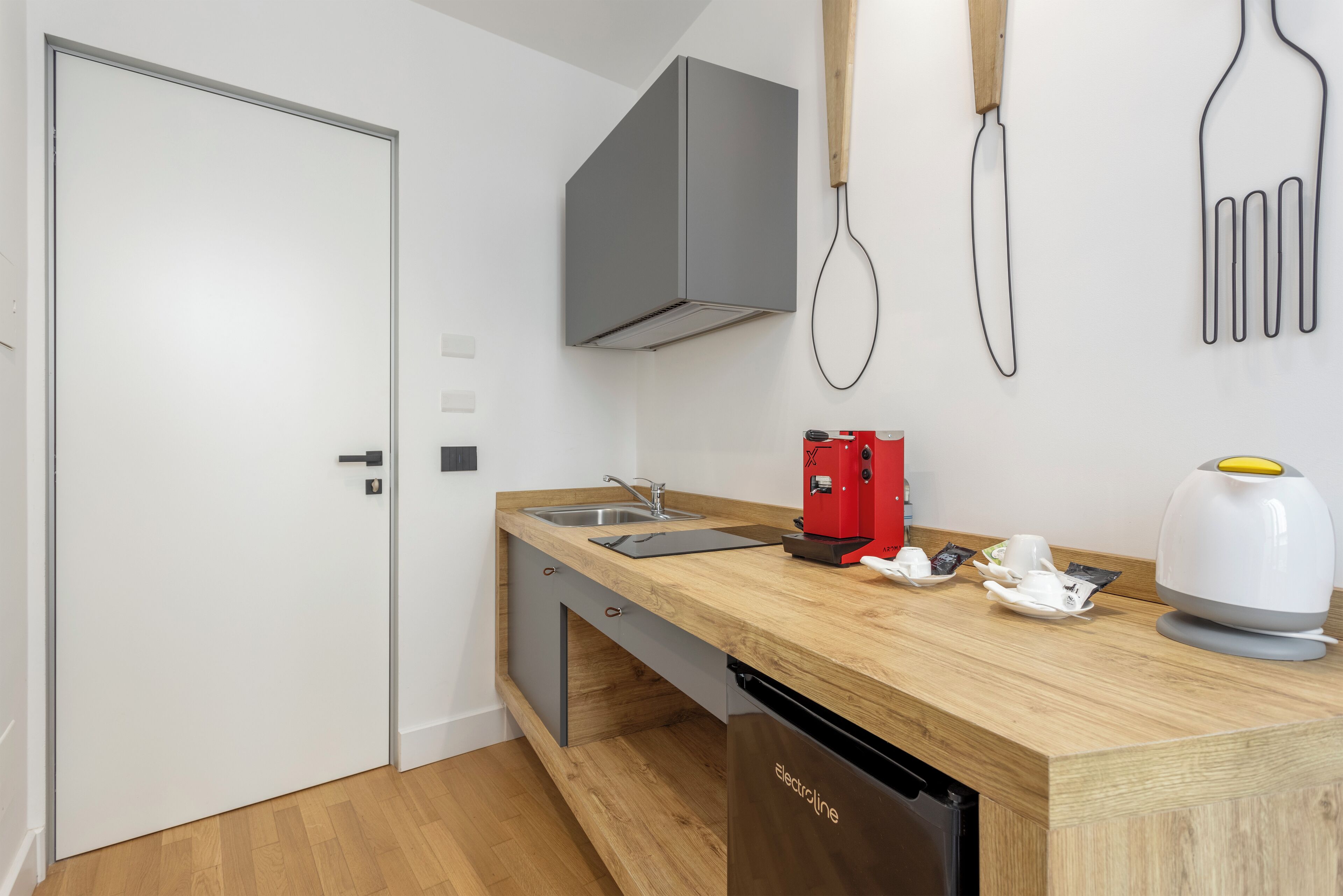A compact kitchen with a wooden countertop, a built-in dishwasher, a red coffee machine, and a kettle.