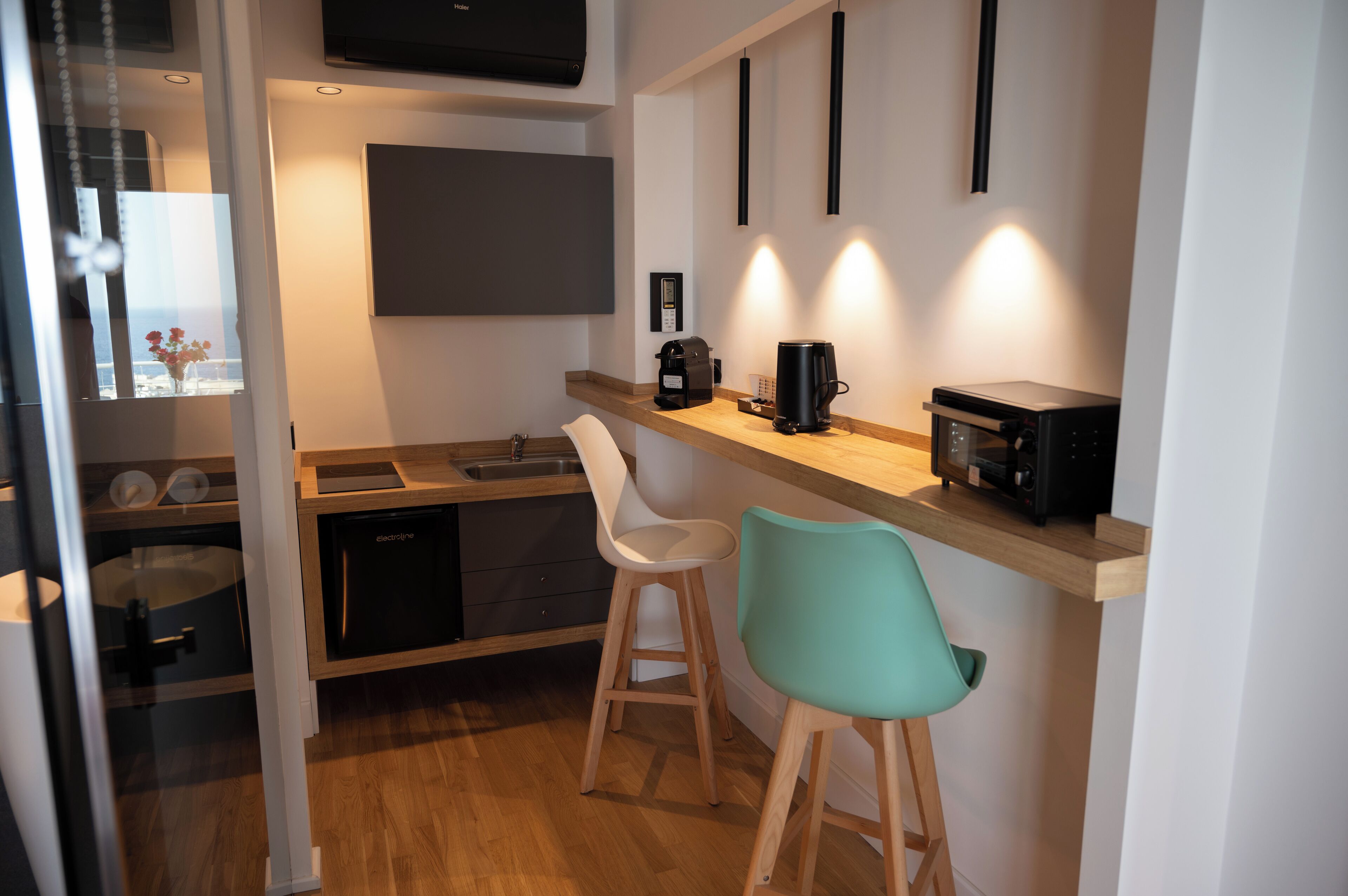 A modern kitchen with a built-in dishwasher, a coffee machine, and a microwave. There are two bar stools and a window with a view.