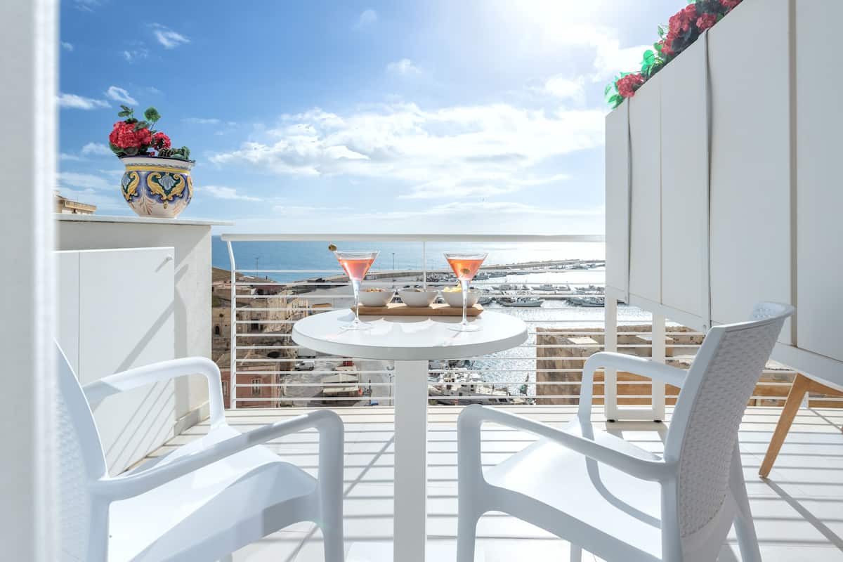 A balcony with white chairs, a round table with two martini glasses, and a decorative vase with flowers.