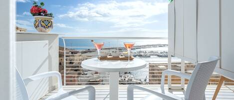 A balcony with white chairs, a round table with two martini glasses, and a decorative vase with flowers.
