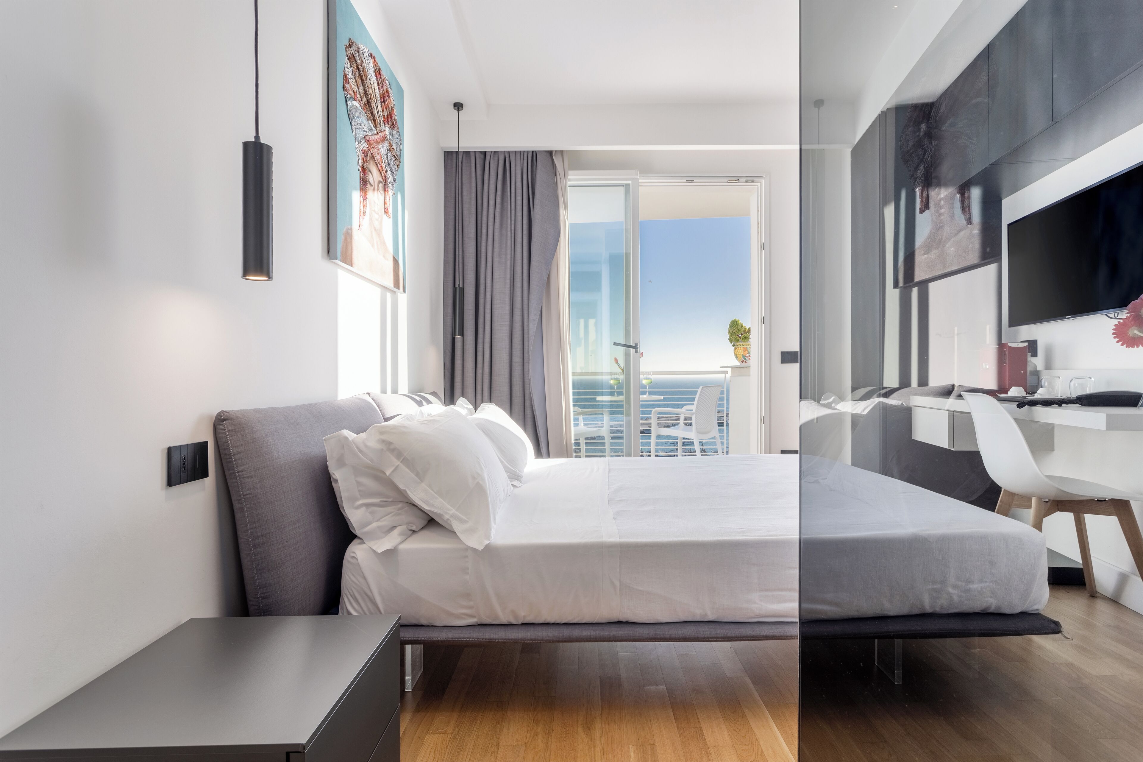 A modern hotel room with a bed, a desk, and a balcony with a view.