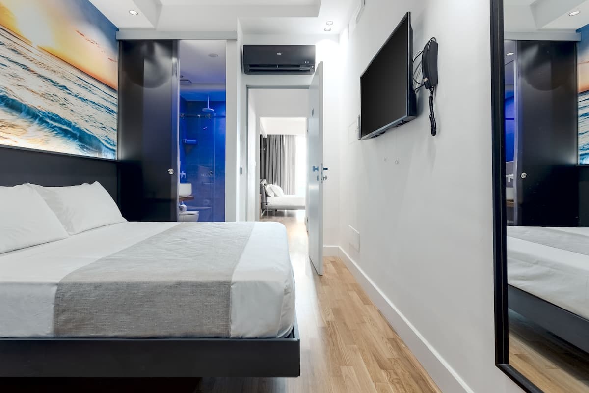 A modern hotel room with a large bed, a flat-screen TV mounted on the wall, and a bathroom visible through an open door.