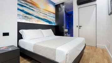 Un dormitorio moderno con una cama grande, una mesita de noche, aire acondicionado instalado en la pared y un baño visible a través de una puerta de vidrio.