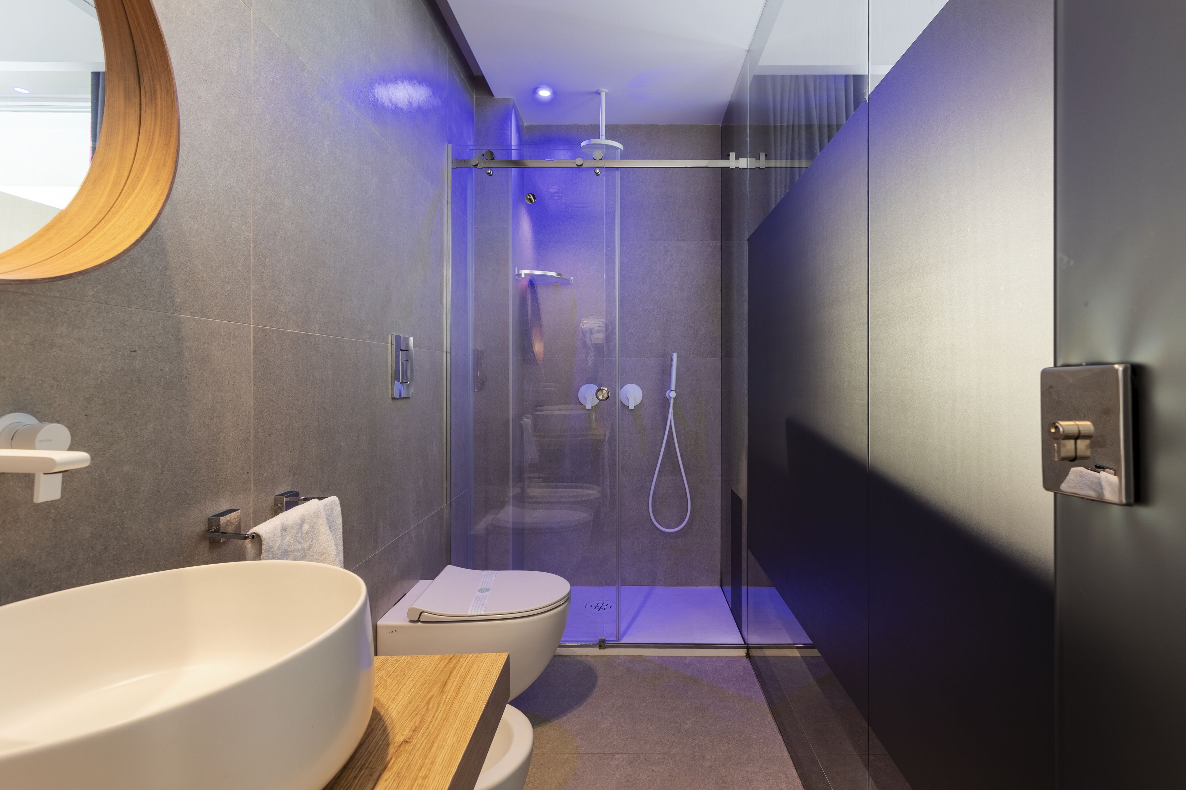 Un baño moderno con un lavabo blanco grande, ducha con cerramiento de vidrio y tocador de madera.