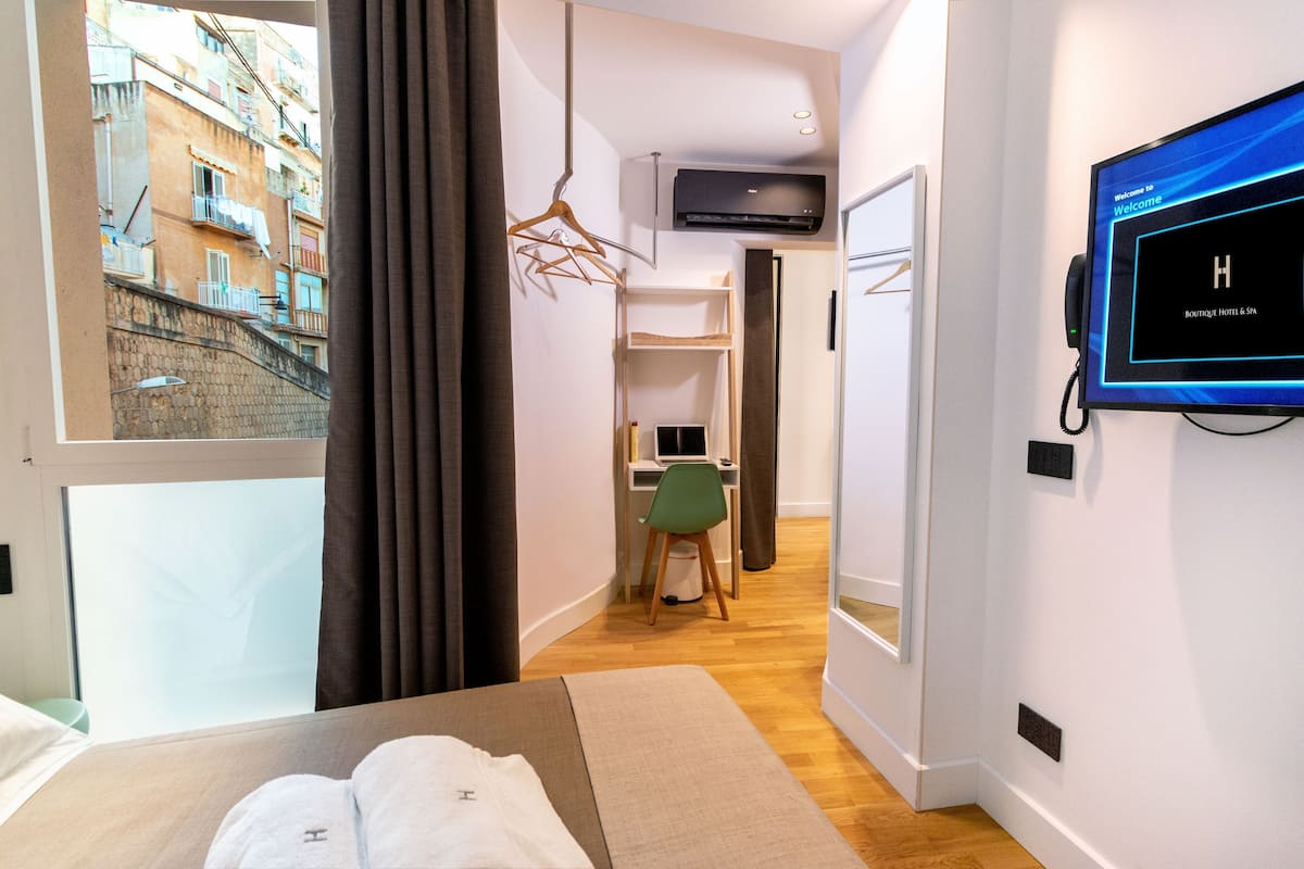 A hotel room with a bed, a desk, a chair, a TV, and a view of the outside.