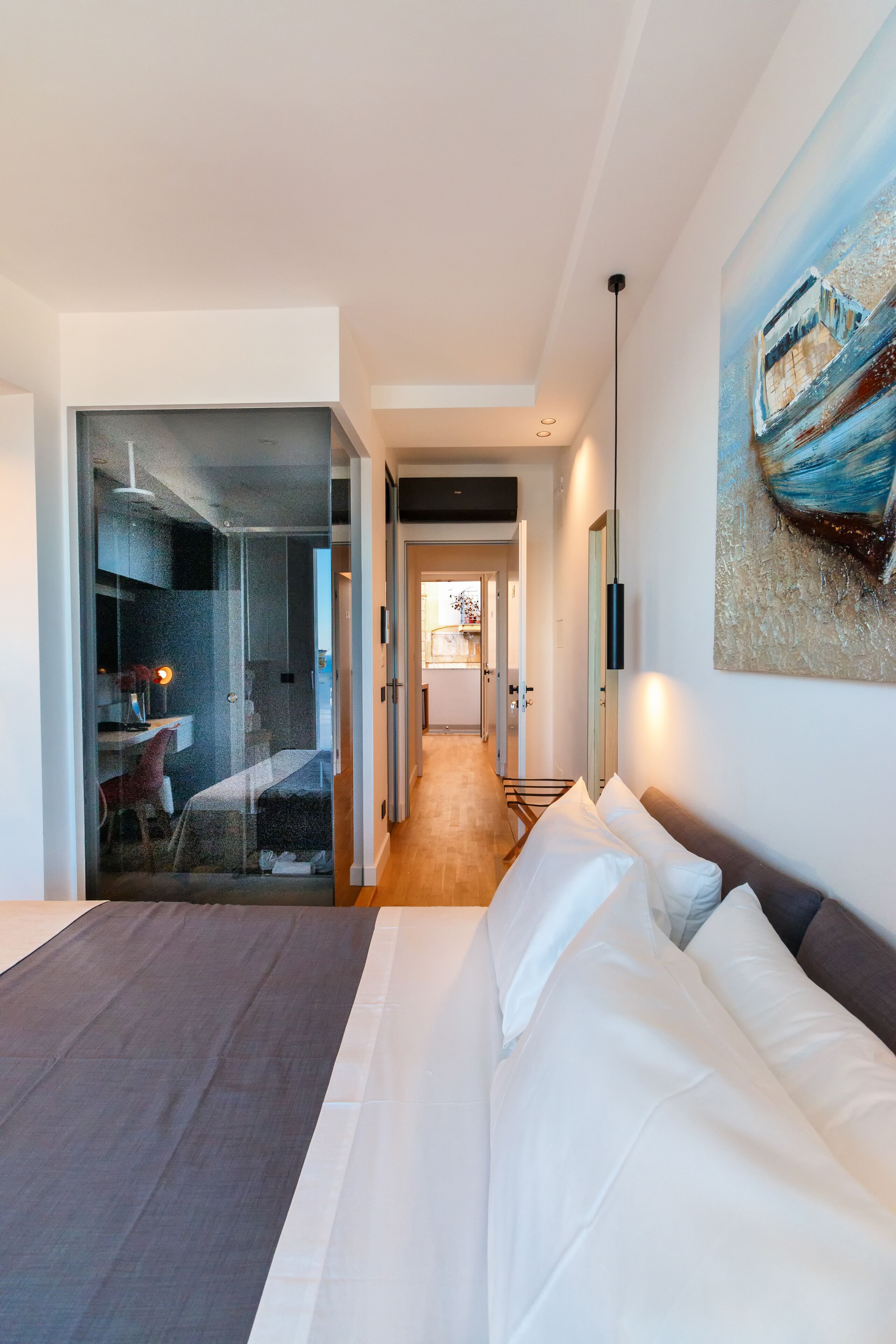 Une chambre d’hôtel moderne dotée d’un grand lit, d’une paroi en verre séparant la chambre à coucher de la salle de bain, et offrant une vue sur la cuisine.