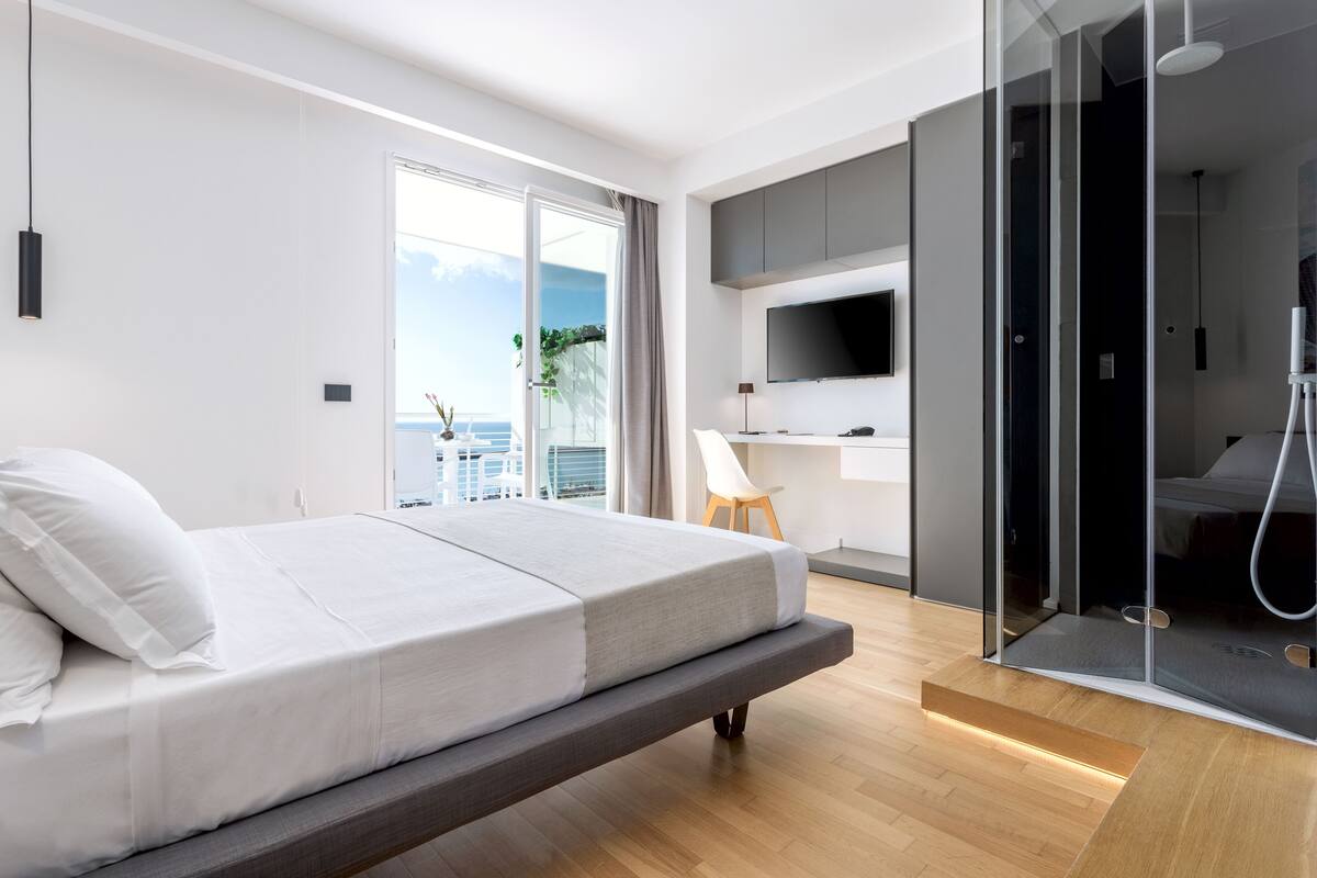A modern bedroom with a bed, a TV, and a shower area.
