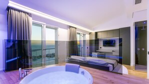 Een moderne slaapkamer met een groot bed, een balkon met glazen wanden, een televisie en een jacuzzi.