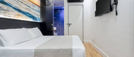 A modern hotel room with a bed, a mounted TV, and a large painting of a sunset over the ocean.