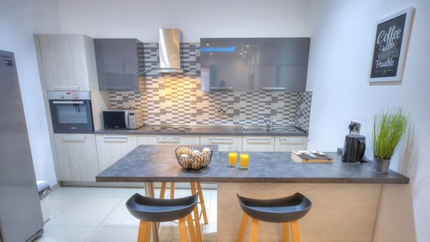 A modern kitchen with a central island, bar stools, a microwave, and a coffee machine. - Tastefully furnished 3beds/3baths, 2balconies WVID1 (Gzira)