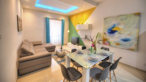 A modern living room with a sofa, a dining table set for four, and a TV. - Tastefully furnished 3beds/3baths, 2balconies WVID1 (Gzira)