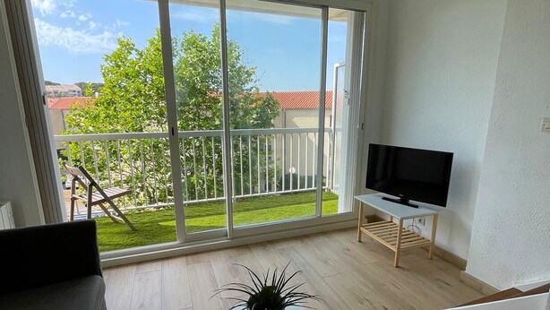 Ein modernes Wohnzimmer mit Balkon, Flachbildfernseher und Topfpflanze.