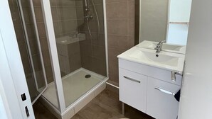 Ein modernes Badezimmer mit einer Duschkabine aus Glas, einem weißen Waschbecken und einem Spiegel darüber.