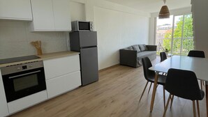 Eine moderne Küche mit weißen Schränken, einem eingebauten Backofen, einer Mikrowelle und einem Kühlschrank. Es gibt einen Essbereich mit einem weißen Tisch und schwarzen Stühlen.