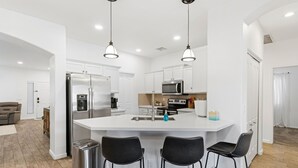 Cozinha moderna com armários brancos, eletrodomésticos de aço inoxidável e uma ilha central com banquetas.