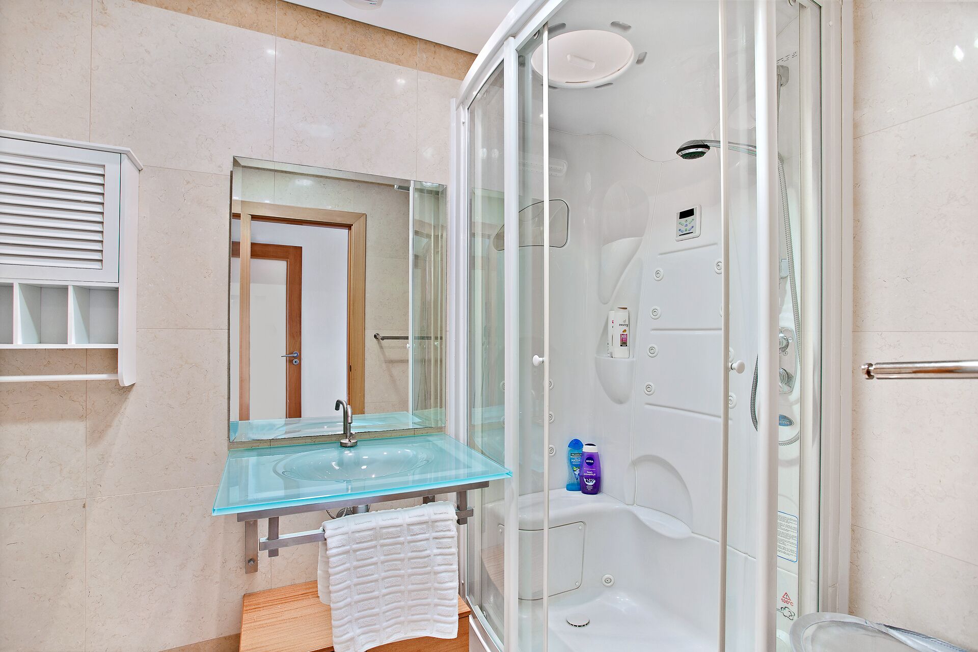 A modern bathroom with a glass shower enclosure, a glass sink, and a wooden vanity.