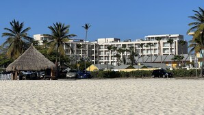 Um hotel à beira-mar com vários andares, palmeiras e uma estrutura com telhado de palha.