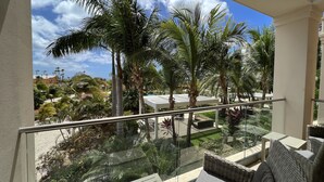 Varanda com mobiliário de vime, guarda-corpo de vidro e vista para palmeiras e uma piscina.