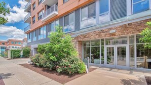 A multi-story building with a mix of brick and glass facade, outdoor seating area, and a well-maintained garden with shrubs and flowers. - Chic 1 bed Apt + Rooftop & Gym - Downtown Stamford (Stamford)