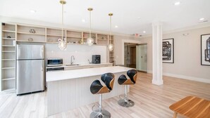 A modern kitchen with a central island, stainless steel appliances, pendant lighting, and a minimalist design. - Chic 1 bed Apt + Rooftop & Gym - Downtown Stamford (Stamford)