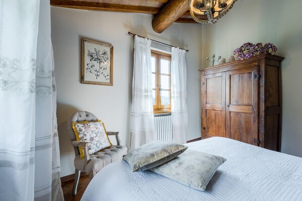 Une chambre à coucher comprenant un lit, une chaise, une armoire en bois et une fenêtre avec des rideaux.
