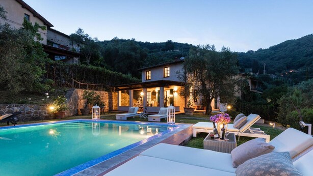 A pool area with lounge chairs and a house in the background. - Villa Arsina in Lucca (Lucca)