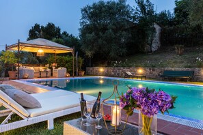 A poolside area with a lounge chair, a covered seating area, and a table with a candle and flowers.