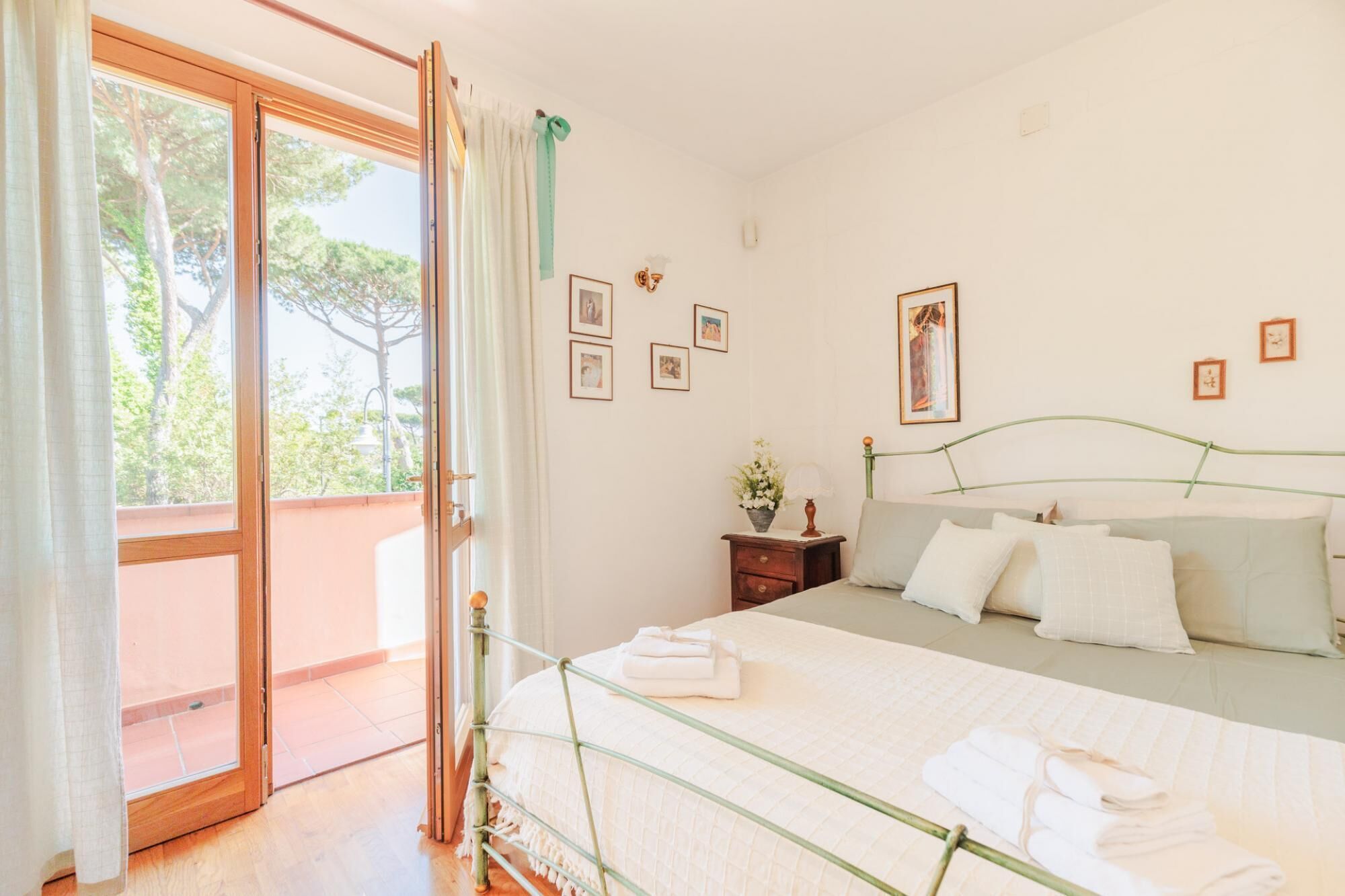 A bedroom with a bed, a nightstand, a window with curtains, and framed pictures on the wall.