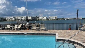 A swimming pool with lounge chairs, a tiled deck, and a view of buildings across the water.