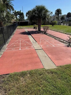A shuffleboard court with markings and a surrounding fence.