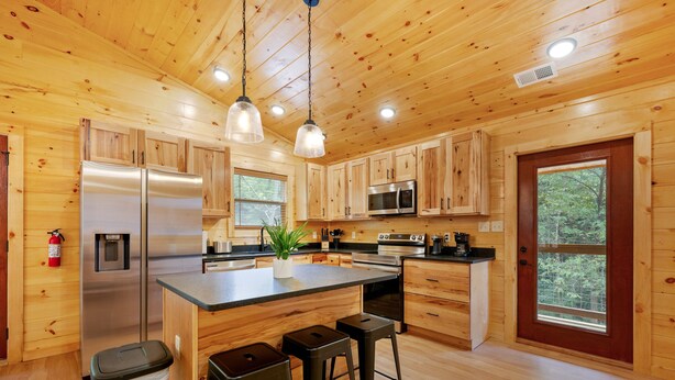 A wooden cabin-style kitchen with a central island, stainless steel appliances, and a large window. - ⛰️Li'l Red Express Cabin in Pigeon Forge🌄Close to Dollywood🎢 & The Island  (Pigeon Forge)