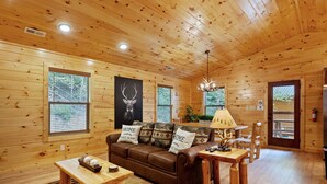 A wooden cabin interior with a brown leather sofa, a dining table, and a chandelier. - ⛰️Li'l Red Express Cabin in Pigeon Forge🌄Close to Dollywood🎢 & The Island  (Pigeon Forge)