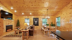 A wooden cabin interior with a fireplace, a sofa, a dining table, and a chandelier. - ⛰️Li'l Red Express Cabin in Pigeon Forge🌄Close to Dollywood🎢 & The Island  (Pigeon Forge)