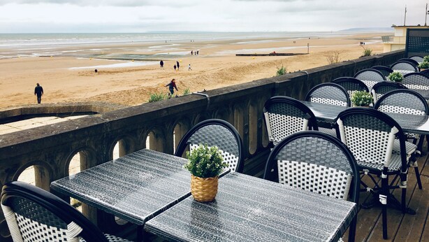 Terraço à beira-mar com mesas e cadeiras, com vista para a praia.