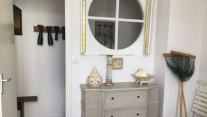 Quarto com penteadeira branca, espelho redondo e mesinha com objetos decorativos.