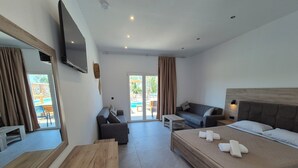Hotelkamer met een bed, een bank, een bureau, een televisie en uitzicht op het zwembad.