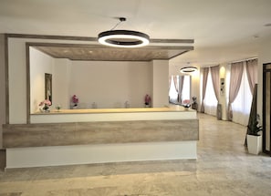 A reception area with a wooden reception desk, a large mirror, and a modern light fixture. - Aegean Pearl (Kos)