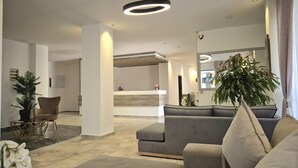 Eine moderne Hotelhalle mit einer Rezeption, einem grauen Sofa, einer Topfpflanze und einem großen Spiegel.