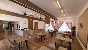 Ein geräumiges Restaurant mit mehreren Tischen, Stühlen, einer Theke mit Speisekarte und einem Deckenventilator.