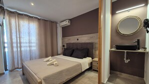 Ein Hotelzimmer mit Bett, Nachttisch, Klimaanlage, Badezimmer mit Waschbecken und Spiegel.
