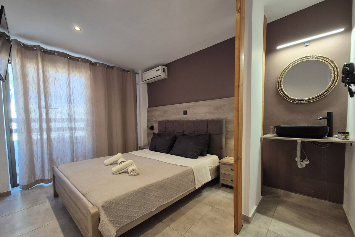 A hotel room with a bed, a bedside table, an air conditioning unit, a bathroom with a sink, and a mirror.
