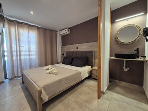 A hotel room with a bed, a bedside table, an air conditioning unit, a bathroom with a sink, and a mirror. - Aegean Pearl (Kos)