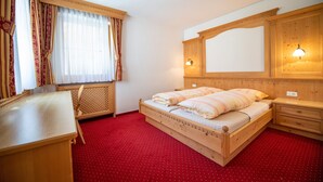 A wooden bed with a headboard, a bedside table, a lamp, and a window with curtains.