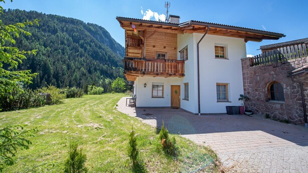 Un chalet à deux étages doté d’un balcon en bois, d’un mur en pierre et d’une allée pavée.