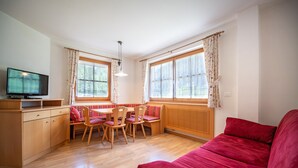 Une pièce avec un canapé rouge, une table à manger en bois avec des chaises, un téléviseur et de grandes fenêtres avec des rideaux.